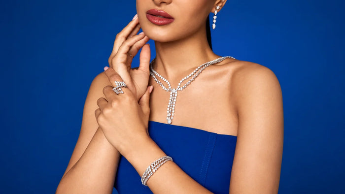 Spectrum Jewels model wearing a diamond necklace, drop earrings, statement ring, and bracelet against a blue backdrop.