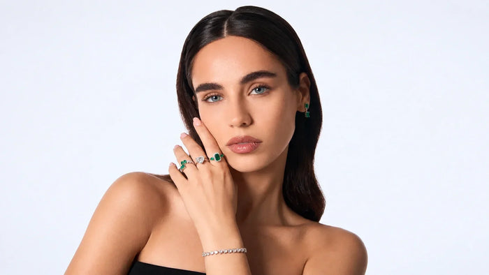 A woman wearing elegant green gemstone earrings and rings with a delicate diamond bracelet from Spectrum Jewels.