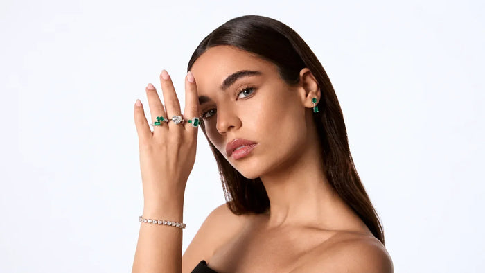 Spectrum Jewels model wearing emerald and diamond rings, emerald earrings, and a diamond bracelet.